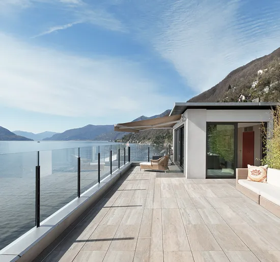 Contemporary retractable awning installed above a spacious tiled patio overlooking a lake